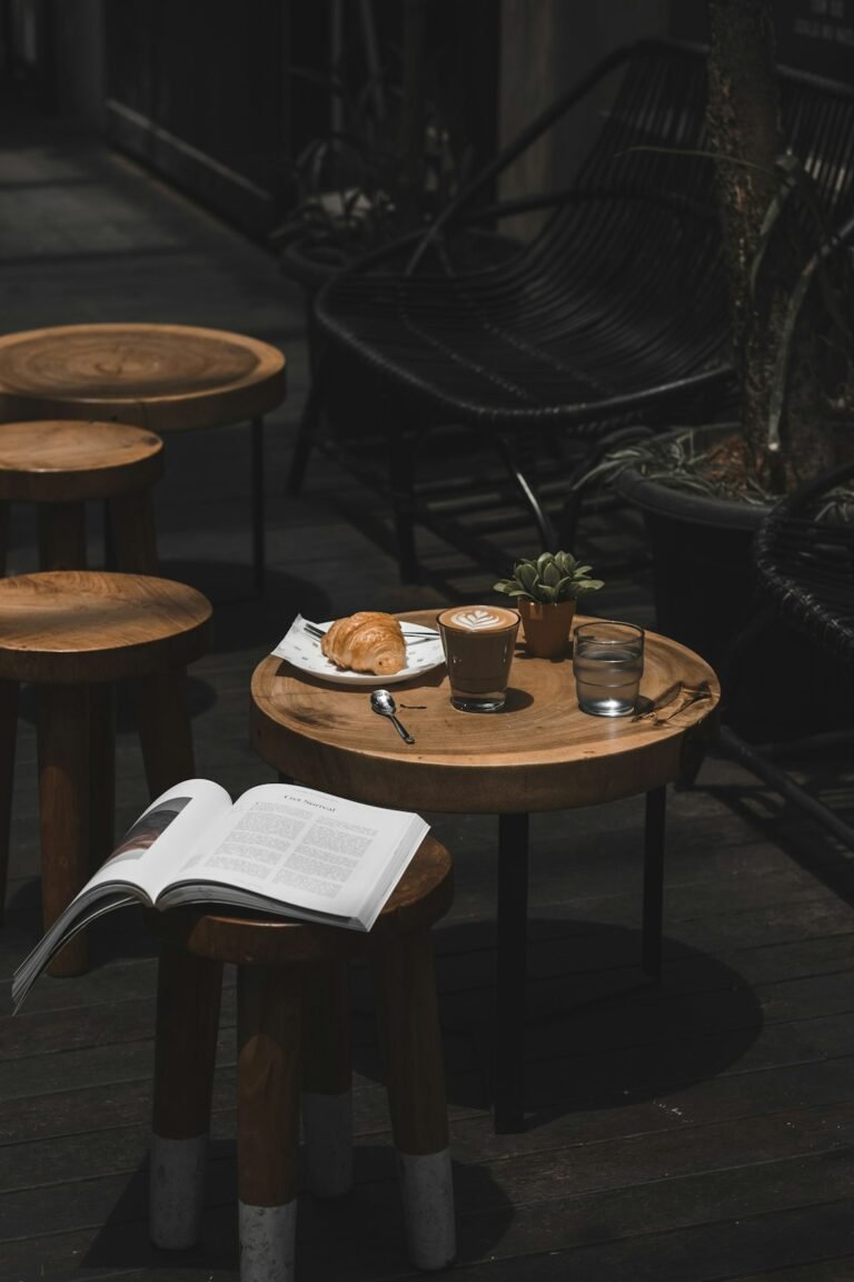 An open book beside a cafe table with coffee and a croissant.
